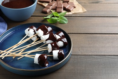 Photo of Delicious marshmallows covered with chocolate on wooden table, space for text