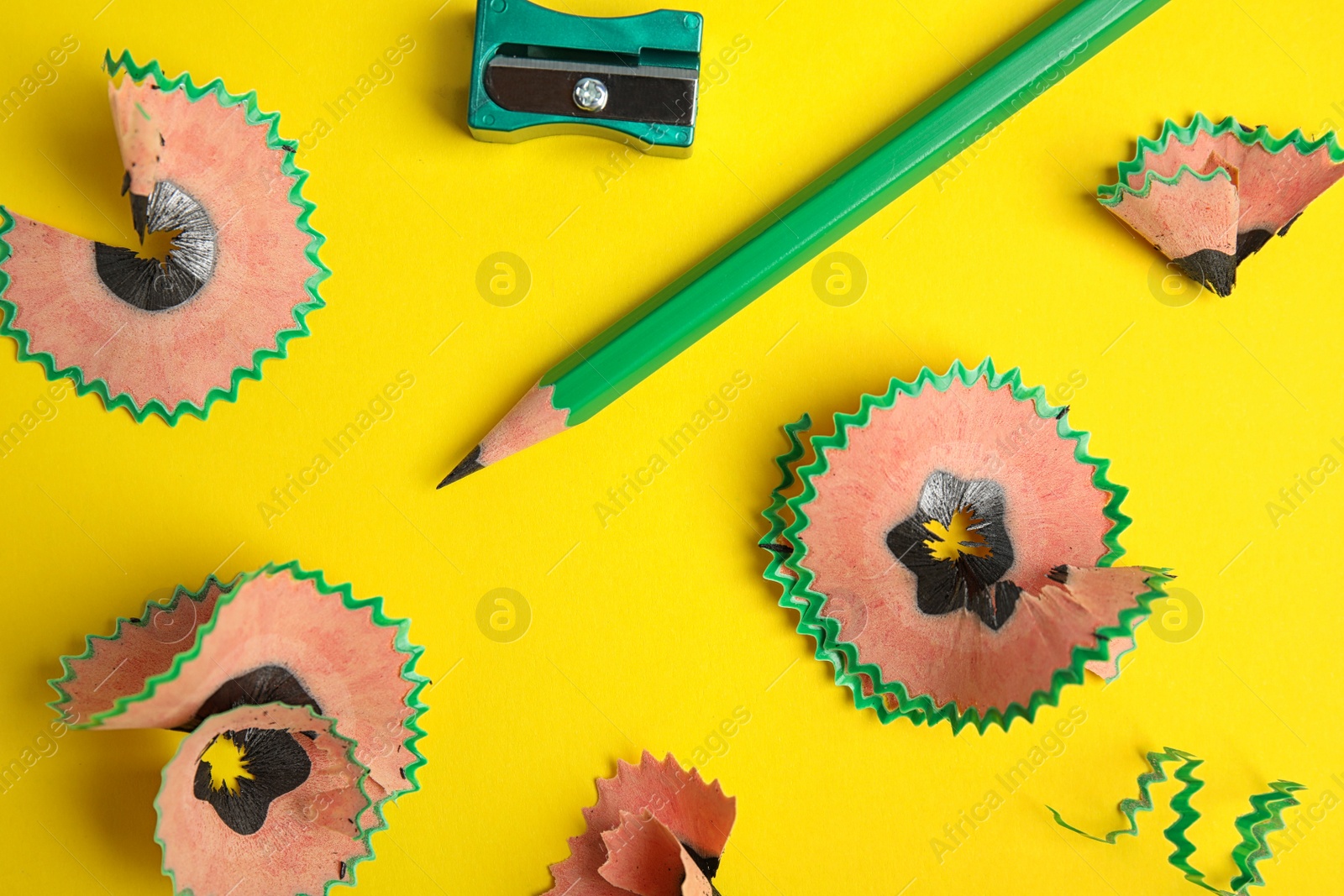 Photo of Pencil, sharpener and shavings on yellow background, top view