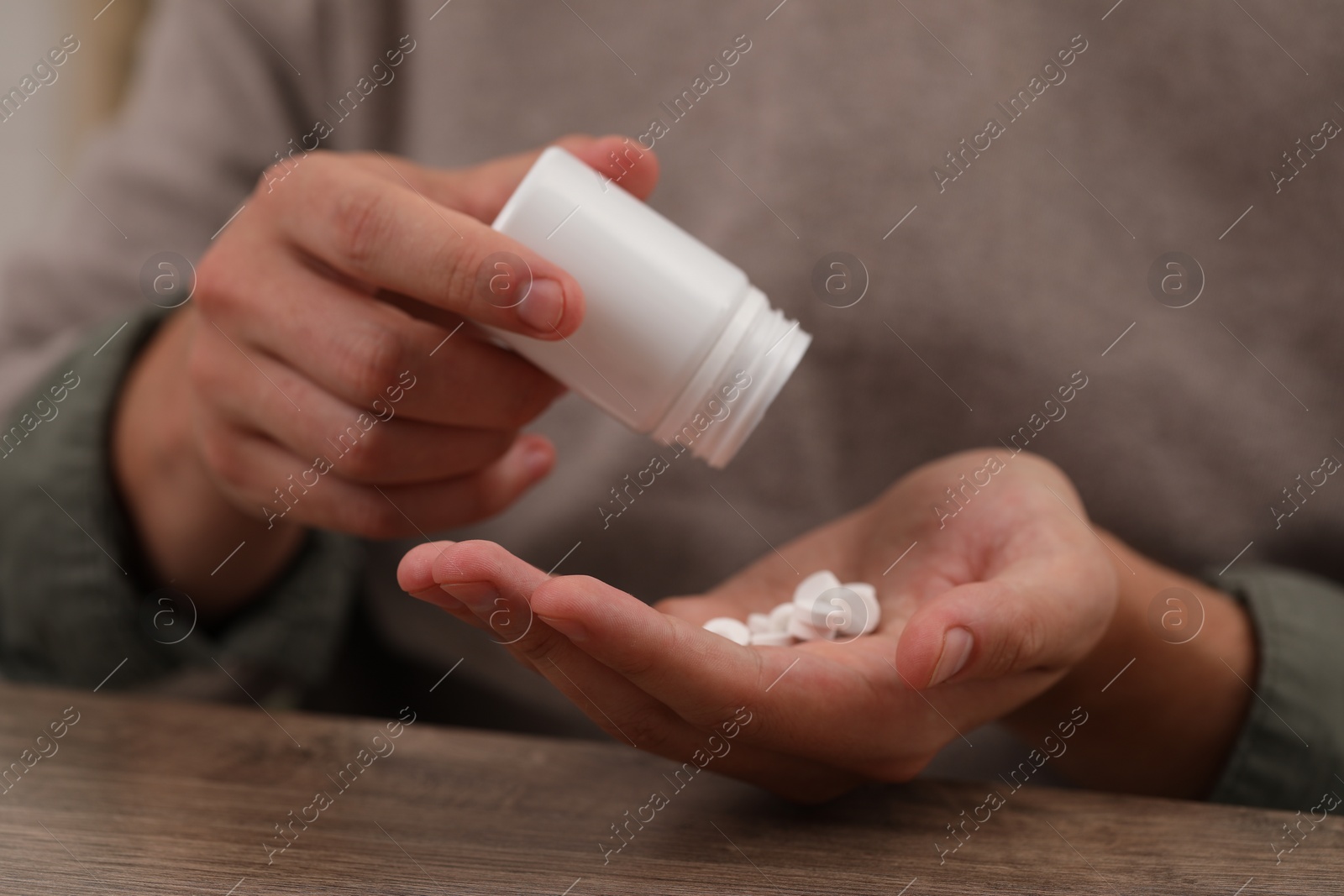 Photo of Man pouring antidepressants from bottle at wooden table, closeup