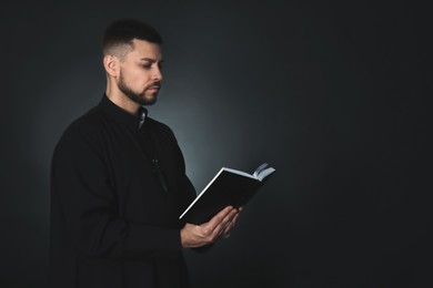 Photo of Priest with Bible praying on dark background, space for text
