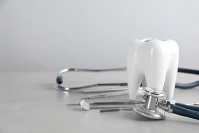 Photo of Tooth shaped holder, set of different dentist's tools and stethoscope on light grey table, closeup. Space for text