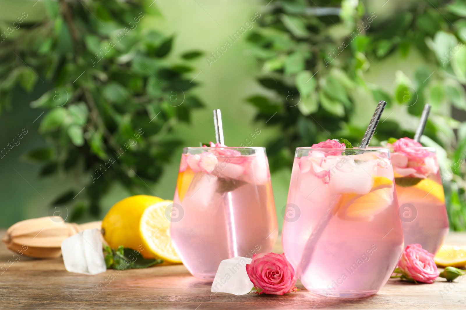 Photo of Delicious refreshing drink with rose flowers and lemon slices on wooden table