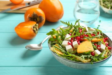 Photo of Delicious persimmon salad with pomegranate and arugula on light blue wooden table