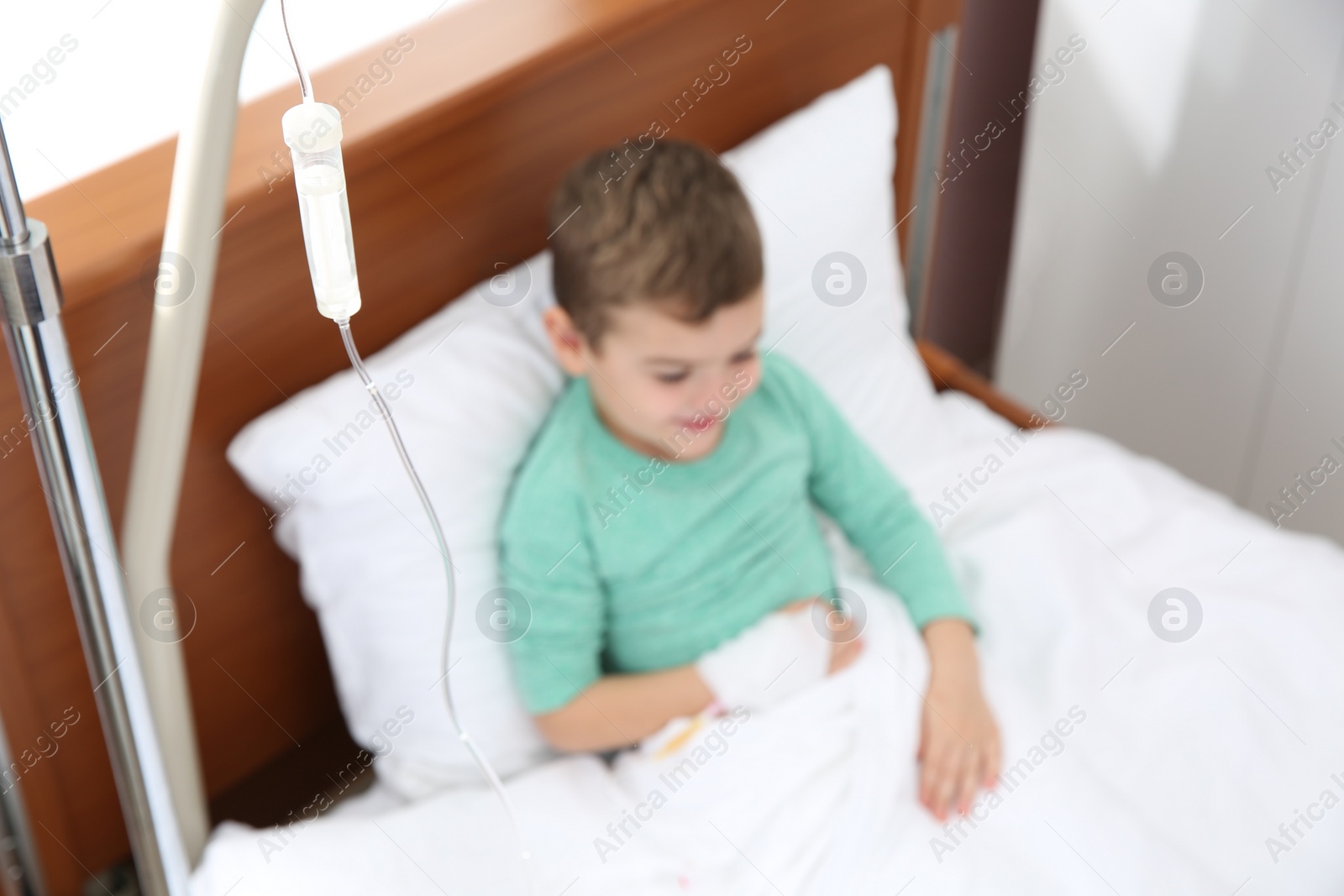 Photo of Little child with intravenous infusion in hospital bed, focus on drip chamber