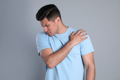 Man suffering from shoulder pain on grey background