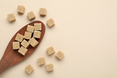 Brown sugar cubes and wooden spoon on beige background, flat lay. Space for text