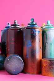 Many spray paint cans with caps on pink background, closeup