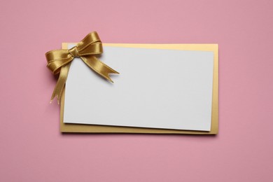 Photo of Blank gift card with golden bow on pink background, top view