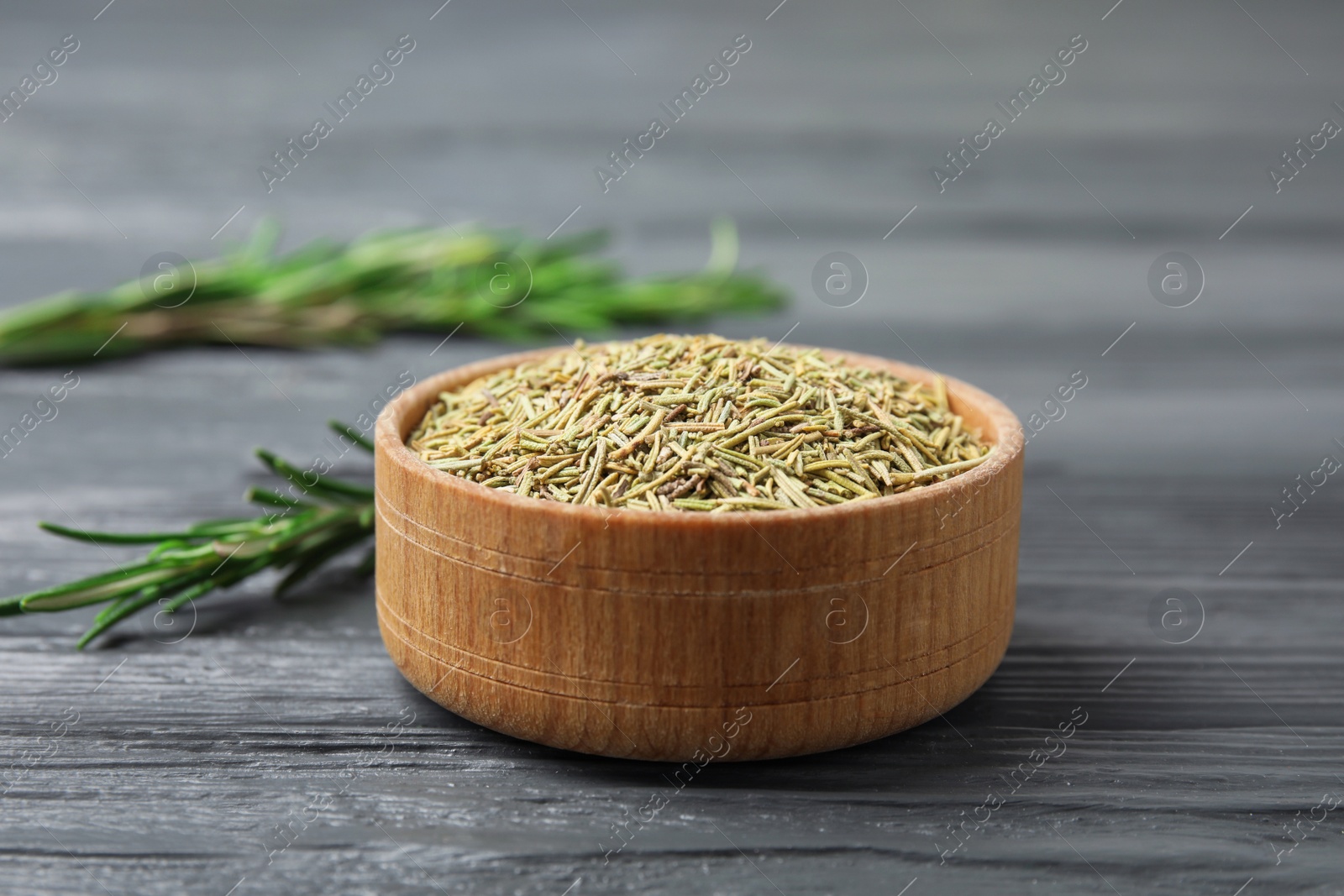 Photo of Wooden bowl of dried rosemary on grey table, space for text