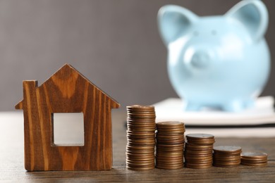 House model, stacked coins, piggy bank and notebook on wooden table, selective focus