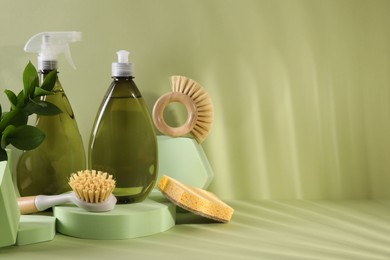 Photo of Bottles of cleaning product, sponge and brushes on light green background. Space for text