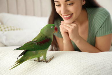 Photo of Young woman with Alexandrine parakeet indoors, closeup. Cute pet