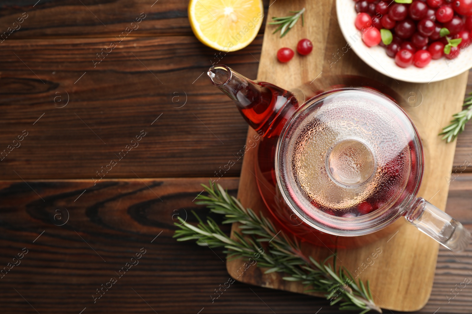 Photo of Tasty hot cranberry tea, lemon, rosemary and fresh berries on wooden table