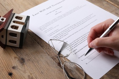 Woman signing Last Will and Testament at wooden table, closeup