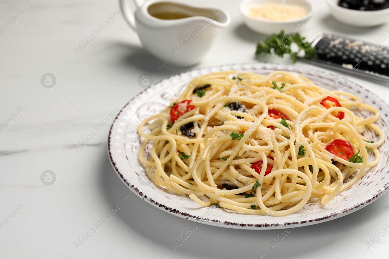 Photo of Delicious pasta with olives, tomatoes and parmesan cheese served on white marble table, closeup
