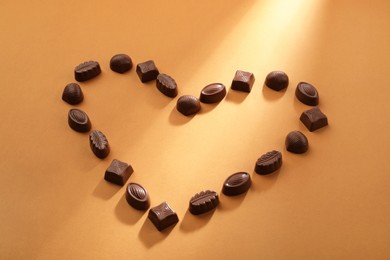 Heart made with delicious chocolate candies on brown background