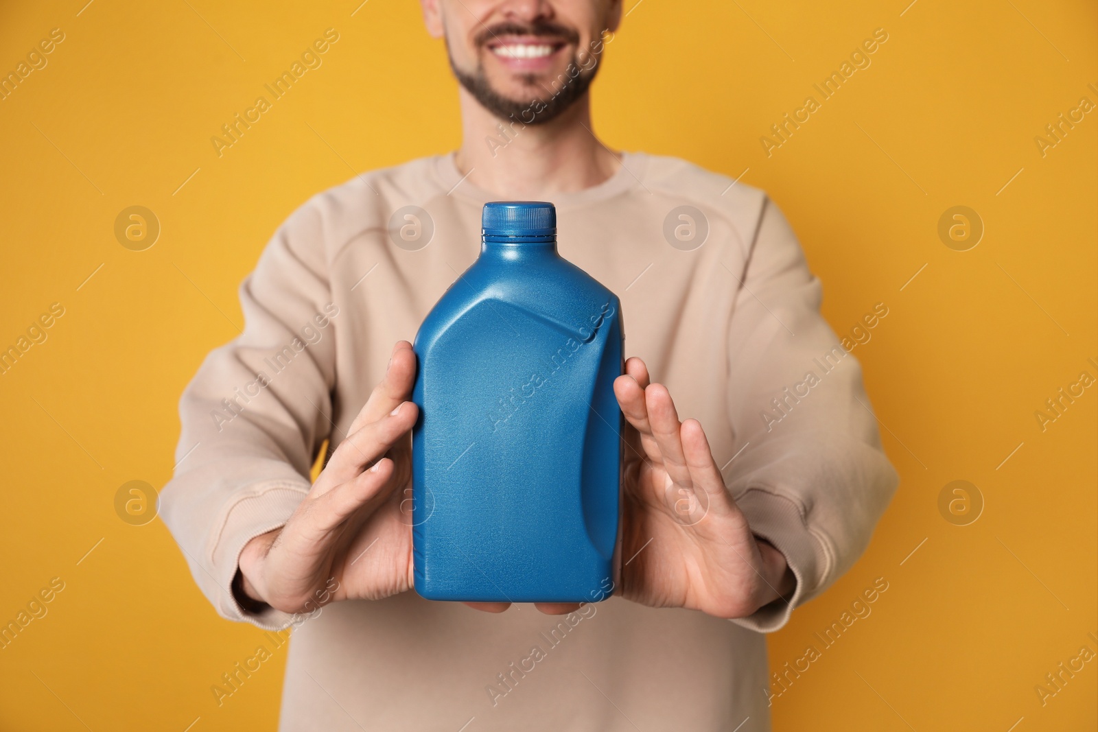 Photo of Man showing blue container of motor oil on orange background, closeup