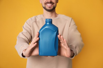 Man showing blue container of motor oil on orange background, closeup