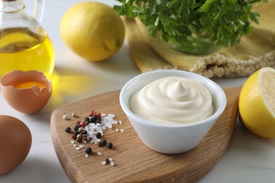 Photo of Tasty mayonnaise sauce in bowl, ingredients and spices on white table, closeup