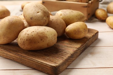 Photo of Raw fresh potatoes and cutting board on light wooden table, closeup