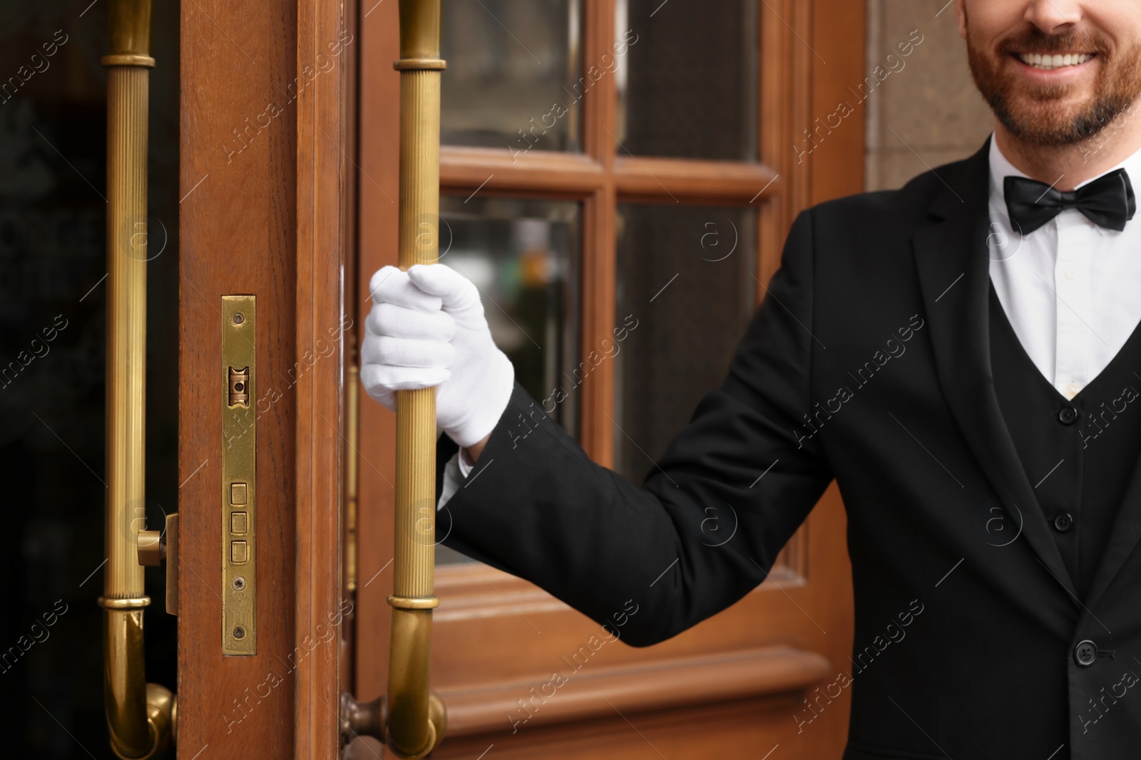 Photo of Butler in elegant suit and white gloves opening hotel door, closeup