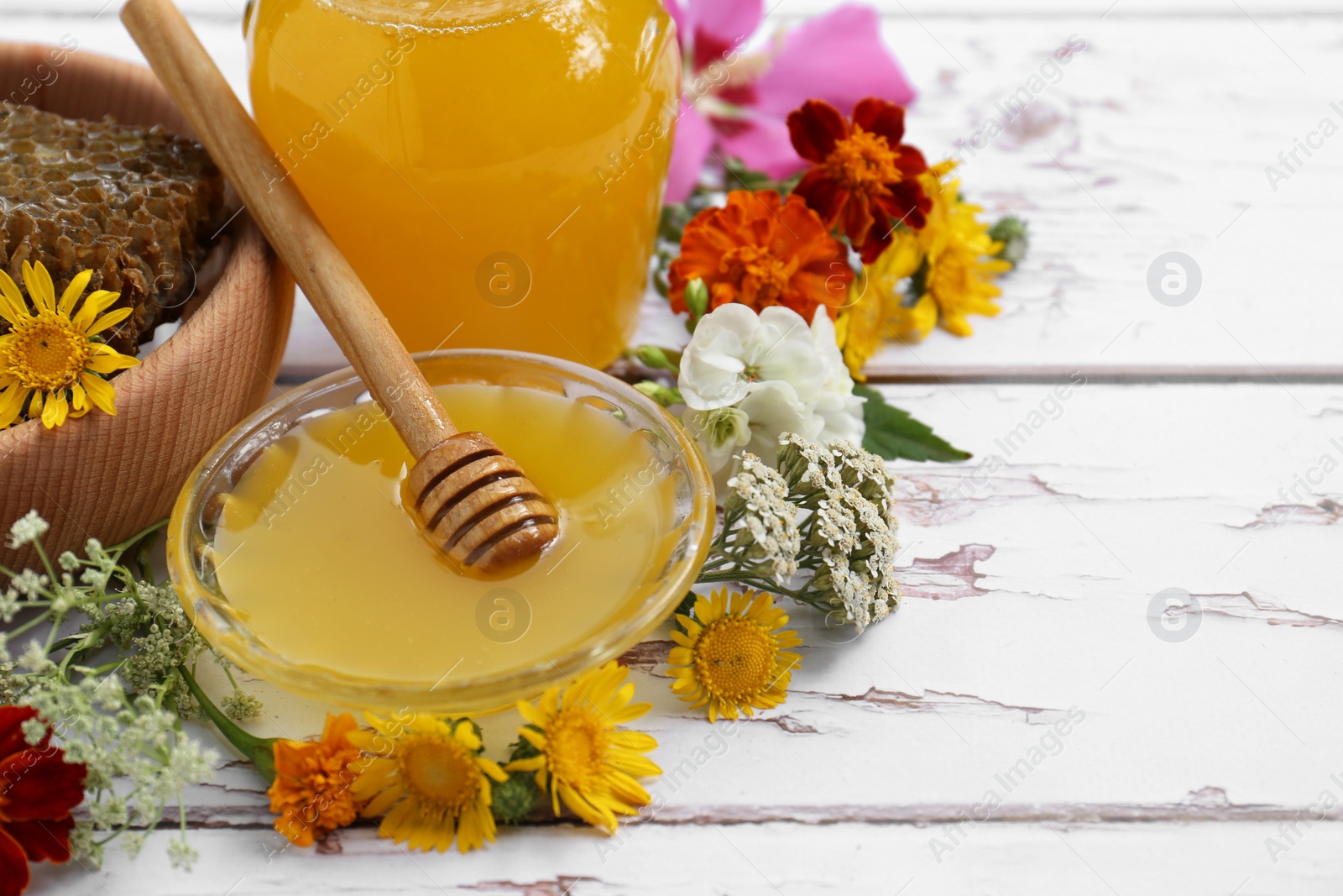 Photo of Delicious honey, combs and different flowers on white wooden table