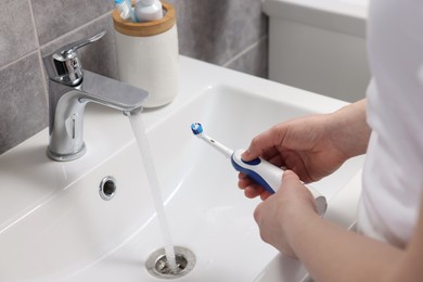 Woman holding electric toothbrush above sink in bathroom, closeup