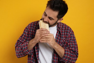 Photo of Young man eating tasty shawarma on yellow background