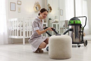 Photo of Professional chambermaid vacuuming pouf in nursery. Cleaning service