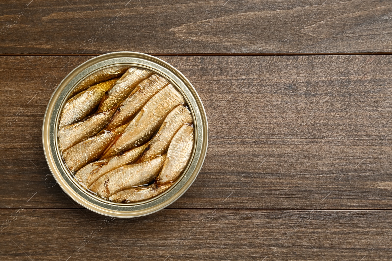 Photo of Sprats in tin can on wooden table, top view. Space for text