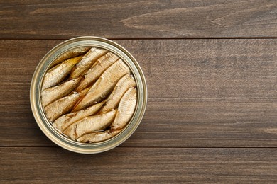 Sprats in tin can on wooden table, top view. Space for text