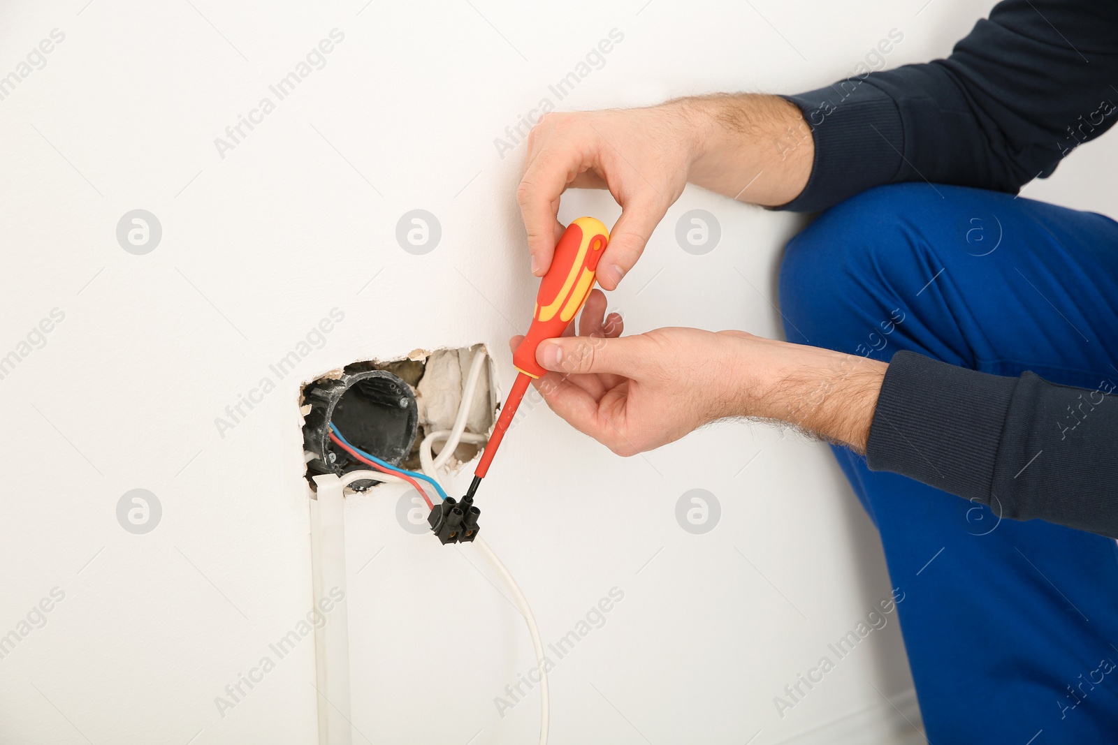 Photo of Electrician with screwdriver repairing power socket indoors, closeup