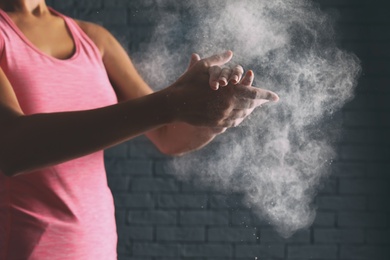 Photo of Young woman applying chalk powder on hands against brick wall