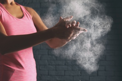 Young woman applying chalk powder on hands against brick wall