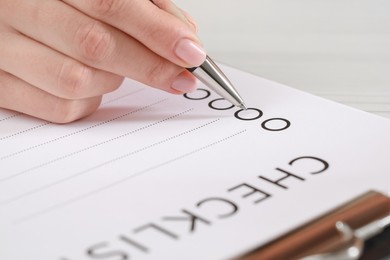 Photo of Woman filling Checklist with pen at table, closeup view