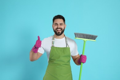 Young man with green broom on light blue background