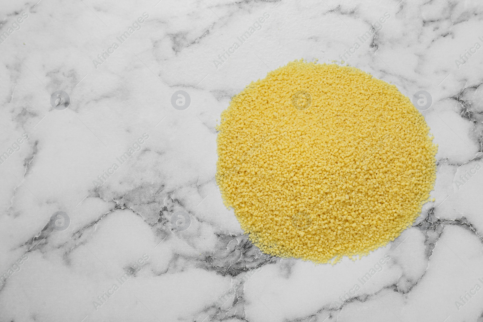 Photo of Heap of raw couscous on white marble table, top view. Space for text