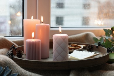 Photo of Tray with burning wax candles and decor on window sill indoors