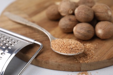 Spoon with grated nutmeg, seeds and grater on white table, closeup