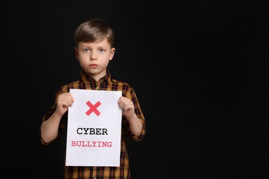 Boy holding sign with phrase Cyber Bullying on black background, space for text