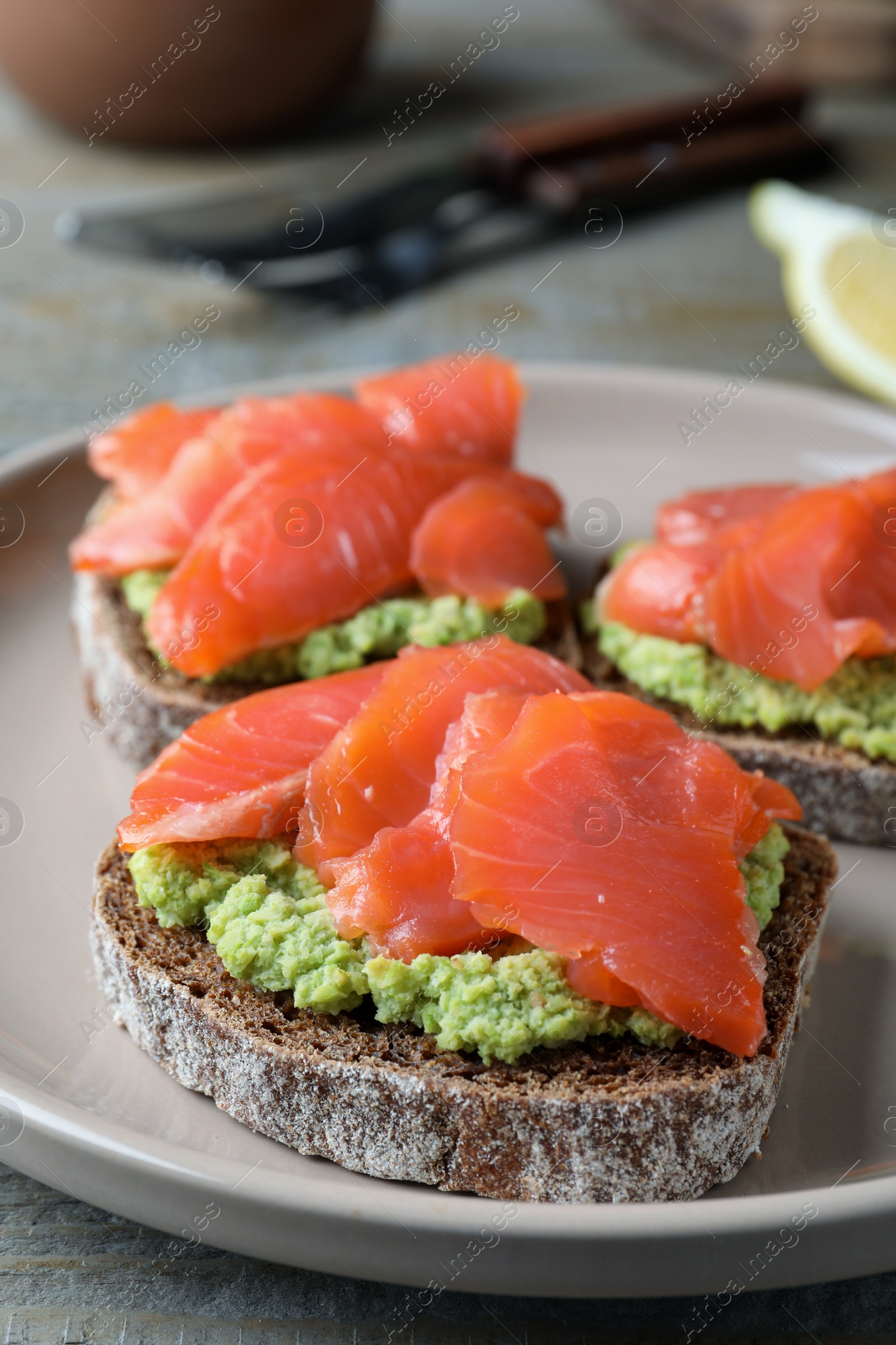 Photo of Delicious sandwiches with salmon and avocado on grey plate, closeup