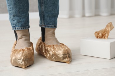 Photo of Woman wearing shoe covers onto her boots indoors, closeup