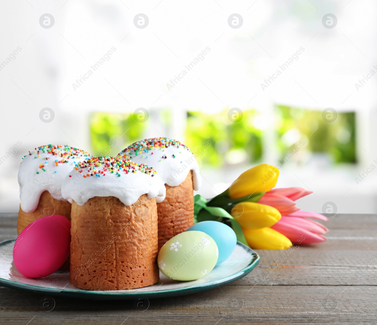Image of Delicious Easter cakes, painted eggs and tulips on wooden table indoors
