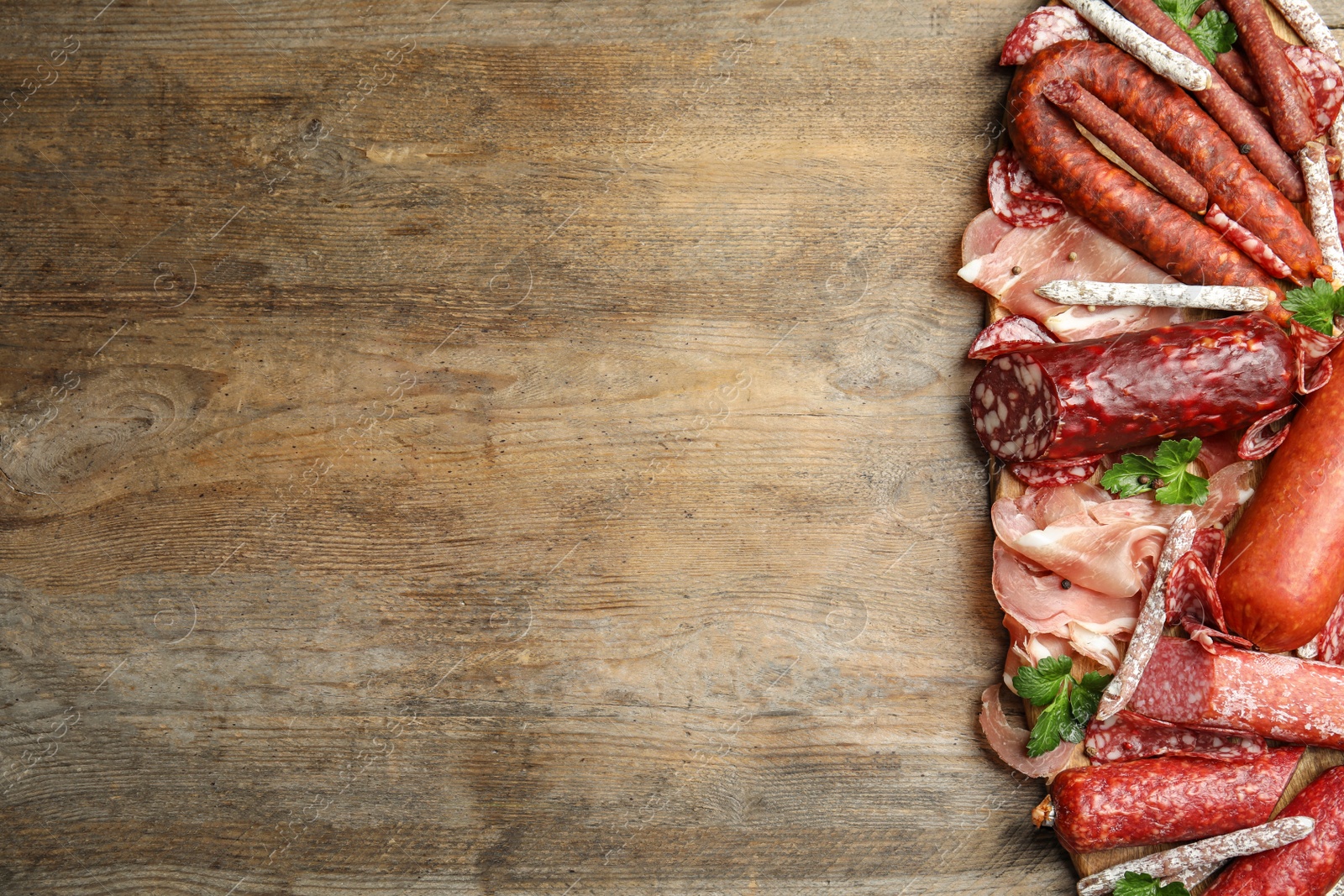 Photo of Different types of sausages with parsley on wooden table, top view. Space for text