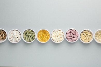 Different vitamin pills in bowls on grey background, flat lay