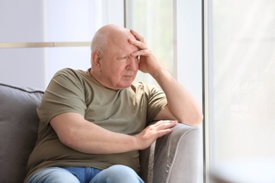 Photo of Depressed senior man sitting in armchair indoors