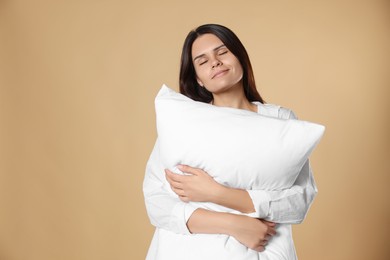 Photo of Sleepy young woman hugging soft pillow on beige background