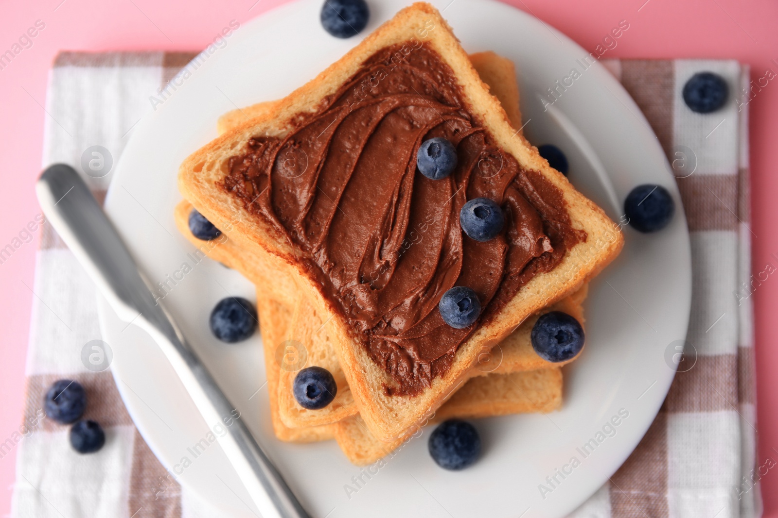 Photo of Tasty toast with chocolate paste and blueberries on pink table, top view