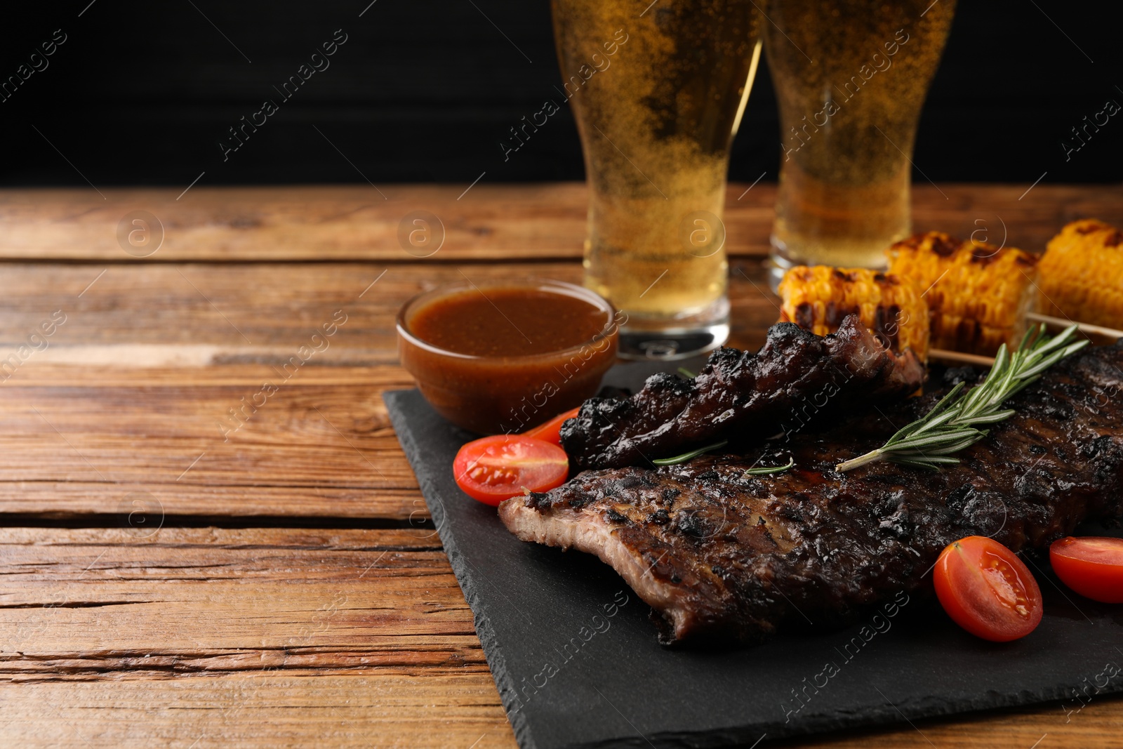 Photo of Glasses of beer, tasty fried ribs, grilled corn and sauce on wooden table. Space for text