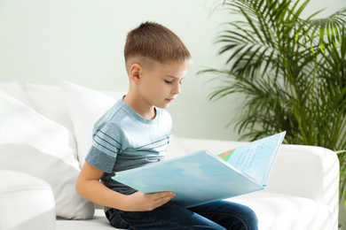 Photo of Little boy reading book on sofa indoors